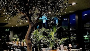 An indoor dining area with tables and chairs, surrounded by potted plants and a large tree. - The Sutherland (Telford)