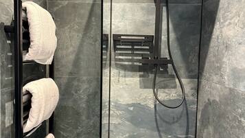 A modern bathroom with a glass shower enclosure, a towel rack with three towels, and a handheld showerhead.