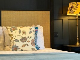 A bed with white linens, a woven headboard, and a floral-patterned pillow.