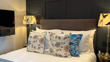 A bed with floral-patterned pillows, a dark headboard, and two lamps on either side.