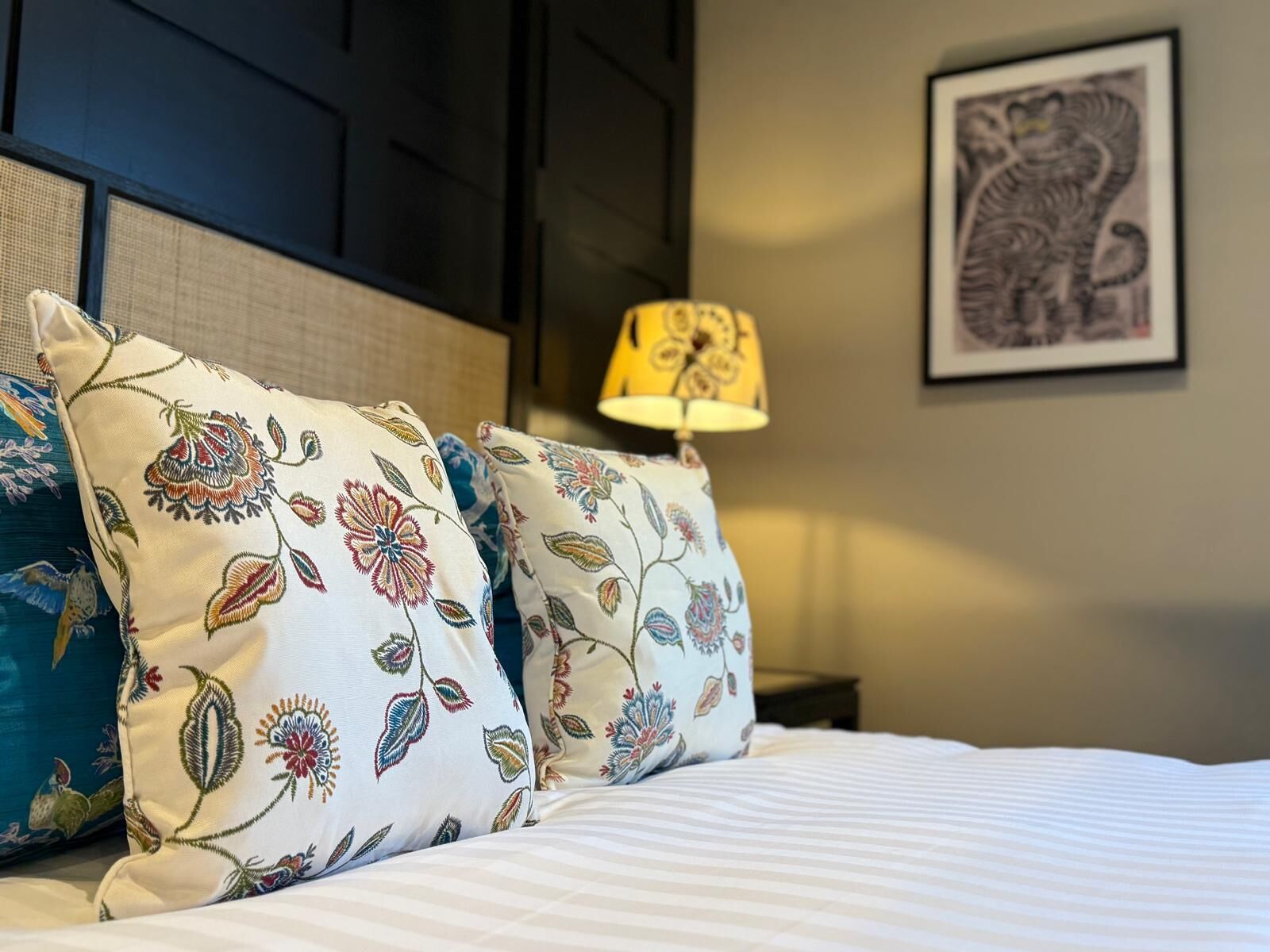 Una cama bien hecha con almohadas estampadas con motivos florales y una obra de arte enmarcada en la pared.