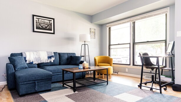 Una sala de estar con un sofá azul, un sillón amarillo, una mesa de centro y un ventanal grande.