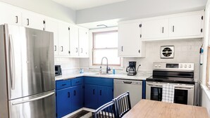 Una cocina moderna con armarios blancos, un refrigerador de acero inoxidable, armarios azules, una mesa de comedor de madera y una estufa negra.