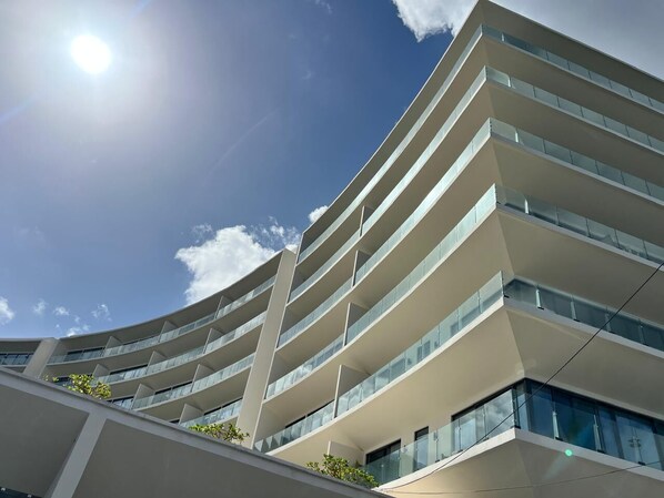 Un immeuble moderne à plusieurs étages, doté d’une façade incurvée, de grandes fenêtres et de balcons.