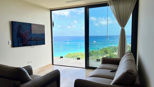 A living room with a large sliding glass door leading to a balcony with a view of the ocean.