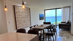 A modern dining area with a wooden table and chairs, a large floral artwork on the wall, and a view of the ocean through large windows.