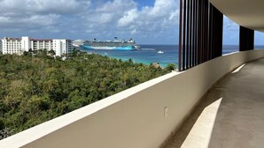 A balcony with a view of a cruise ship, ocean, and buildings in the background.