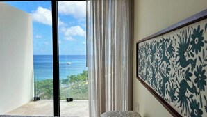 A room with a large window overlooking a scenic ocean view, a patterned bed, and a decorative wall panel.