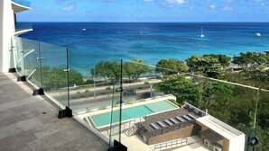 A balcony with a clear view of the ocean and a pool area.