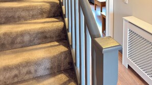 A staircase with carpeted steps and a metal handrail, leading to a room with a radiator and a framed artwork on the wall. - Spacious, entire 3 bedroom house in Wool (The Purbecks) (Wool)