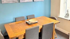 A dining area with a wooden table, grey upholstered chairs, and three landscape paintings on the wall. - Spacious, entire 3 bedroom house in Wool (The Purbecks) (Wool)