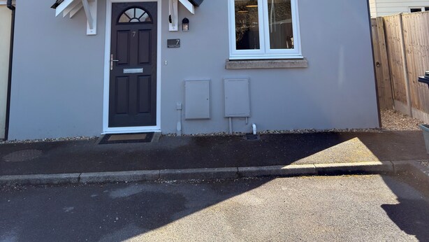 A two-story house with a dark front door, a small porch, and a garage door. - Spacious, entire 3 bedroom house in Wool (The Purbecks) (Wool)