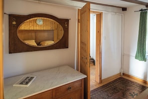 Une pièce avec une coiffeuse en bois, un miroir, une petite table sur laquelle se trouve un livre, une porte en bois et un rideau vert.