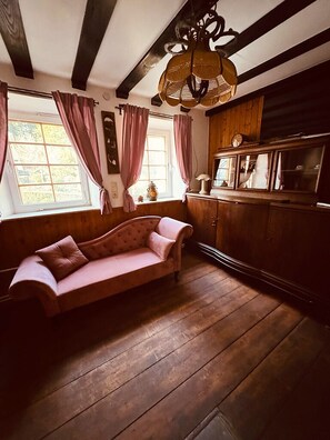 A room with a wooden floor, a pink sofa, a cabinet with glass doors, and a hanging light fixture.