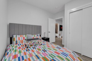 A modern bedroom with a large bed, a grey headboard, a colorful striped bedspread, a bedside table, and a white wardrobe. - Pivate Family Friendly 2-Bedroom Suite near South Health Campus in Calgary (Calgary)