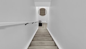 Een smalle trap met houten treden en witte muren, leidend naar een kamer met een ronde spiegel aan de muur.