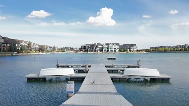 Een steiger aan het water met boten, een heldere lucht en woongebouwen op de achtergrond.
