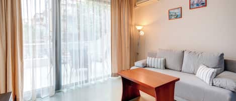 Una sala de estar moderna con un sofá, una mesa de centro de madera, cortinas translúcidas y dos cuadros en la pared.