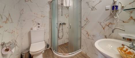 Un baño con inodoro, ducha con mampara de vidrio, lavamanos y paredes con diseño de mármol.