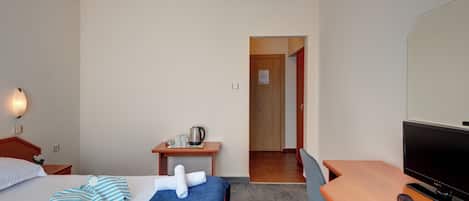 Una habitación de hotel con una cama, un escritorio, un televisor y una puerta que da a otra estancia.