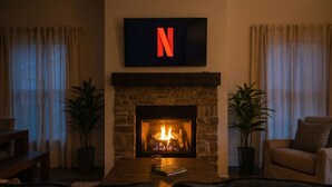 Ein Wohnzimmer mit Kamin aus Stein, dem Netflix-Logo darüber und einem Sofa.