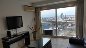 A modern living room with a flat-screen TV, a coffee table, and a leather sofa. A large window offers a city view. - EXTRAORDINARY LOFT in Cordoba 22C (Córdoba)