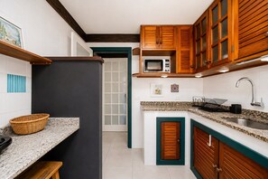 Une cuisine équipée d’un four à micro-ondes, de placards en bois, d’un évier et d’un panier posé sur le plan de travail.