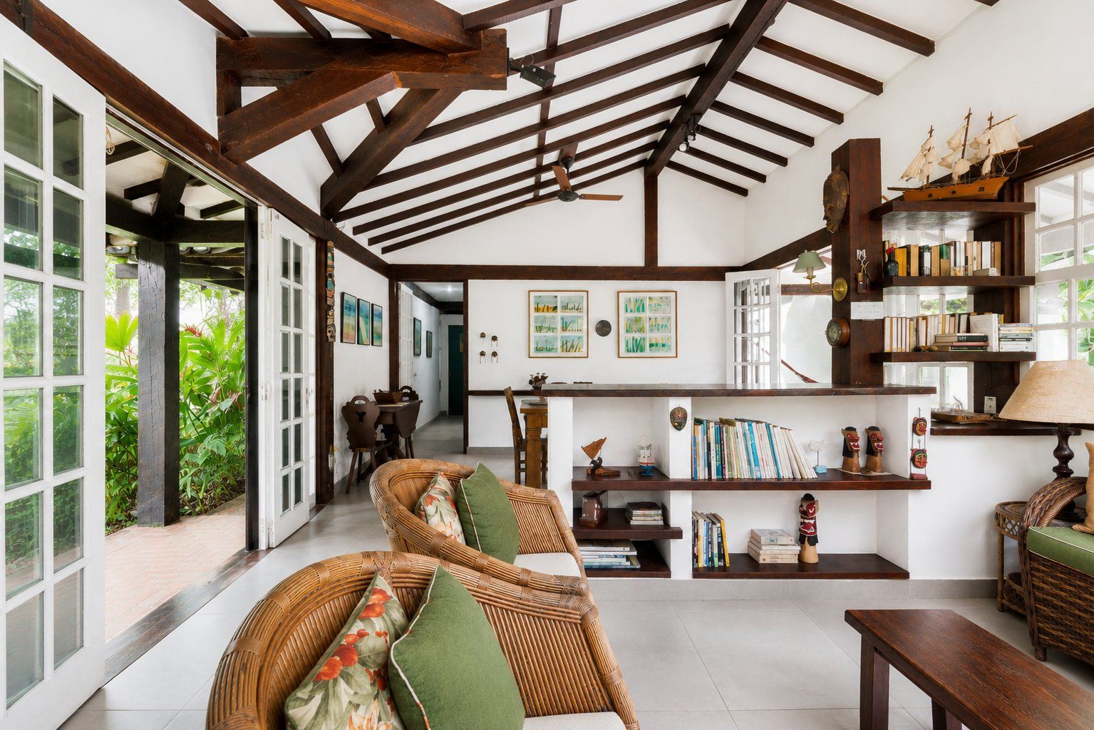 A spacious room with a high ceiling, exposed wooden beams, a dining area, and a bookshelf filled with books and decorative items.
