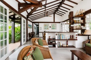 Une pièce spacieuse avec un plafond haut, des poutres apparentes, un coin repas et une bibliothèque remplie de livres et d’objets décoratifs.
