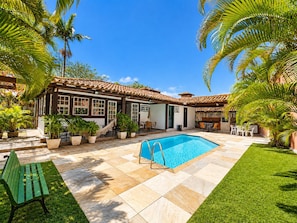 Una casa con piscina, rodeada de palmeras y un césped cuidado.