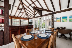 Un comedor con una mesa de madera dispuesta para seis personas, una cocina con armarios de madera y vistas a través de amplios ventanales.
