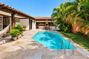 Una piscina con bordeado de azulejos, rodeada de plantas en macetas y mobiliario de exterior.