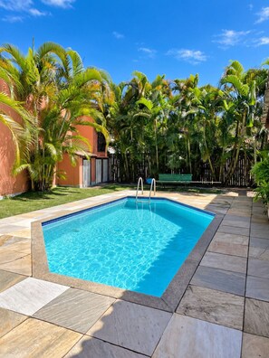 Une piscine rectangulaire bordée de carreaux, entourée de palmiers et dotée d’une terrasse également carrelée.