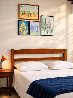 Un lit bien fait, avec du linge de lit blanc et un plaid bleu, une tête de lit en bois et une table de chevet avec une lampe.