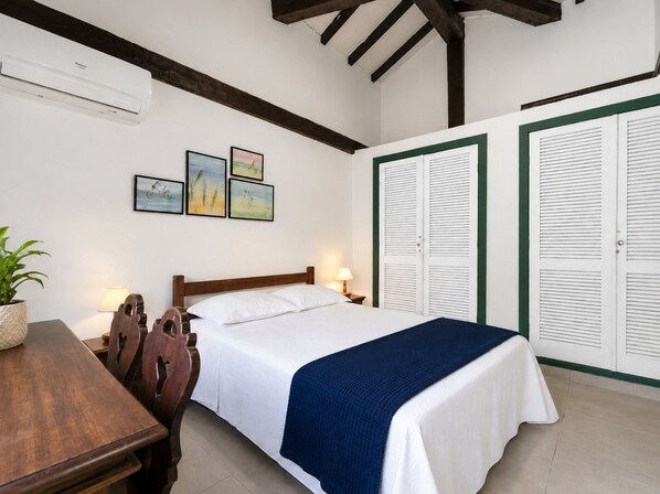 Habitación de hotel con cama, escritorio, silla, planta en maceta y pared decorada con tres cuadros.