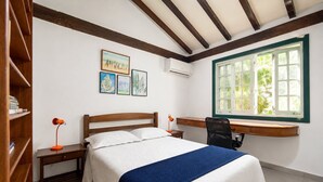 Un dormitorio con cama, escritorio, silla, estantería y ventana con vistas al verdor.