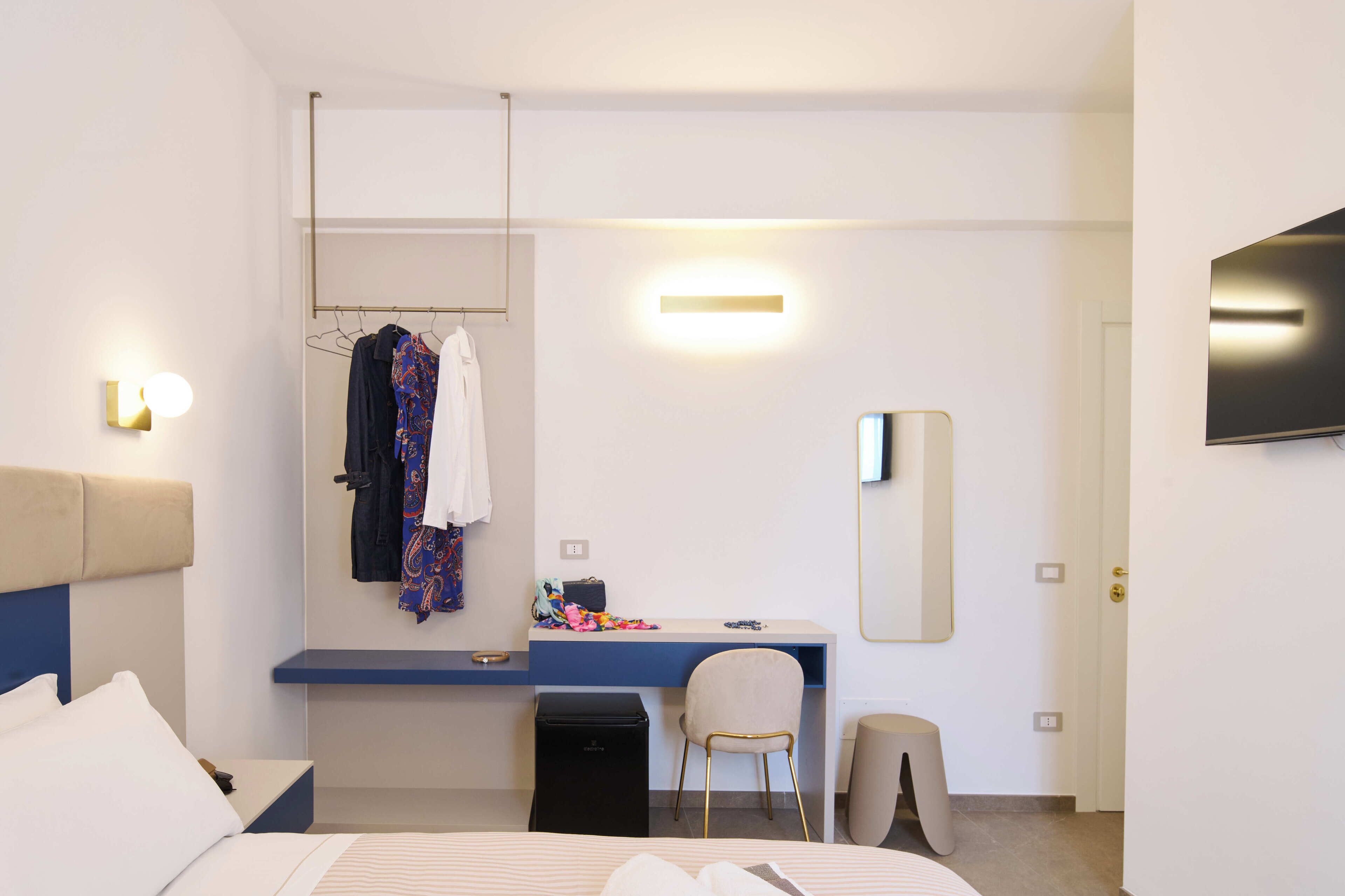 Una habitación de hotel con cama, escritorio, silla, armario, espejo y televisión.