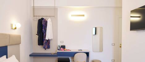 A hotel room with a bed, a desk with a chair, a wardrobe, a mirror, and a television.