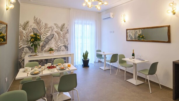 A modern dining area with a white table, green chairs, and a potted plant. - San Nicola Rooms Siracusa (Syracuse)
