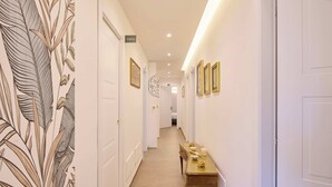 A hallway with white walls, a wooden bench, framed pictures, and a sign indicating the direction to the toilet. - San Nicola Rooms Siracusa (Syracuse)