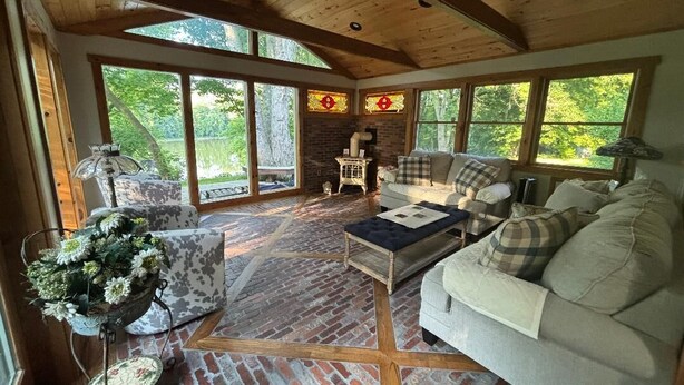 Una sala de estar acogedora con piso de ladrillo, vigas de madera en el techo y amplias ventanas con vistas al exterior.
