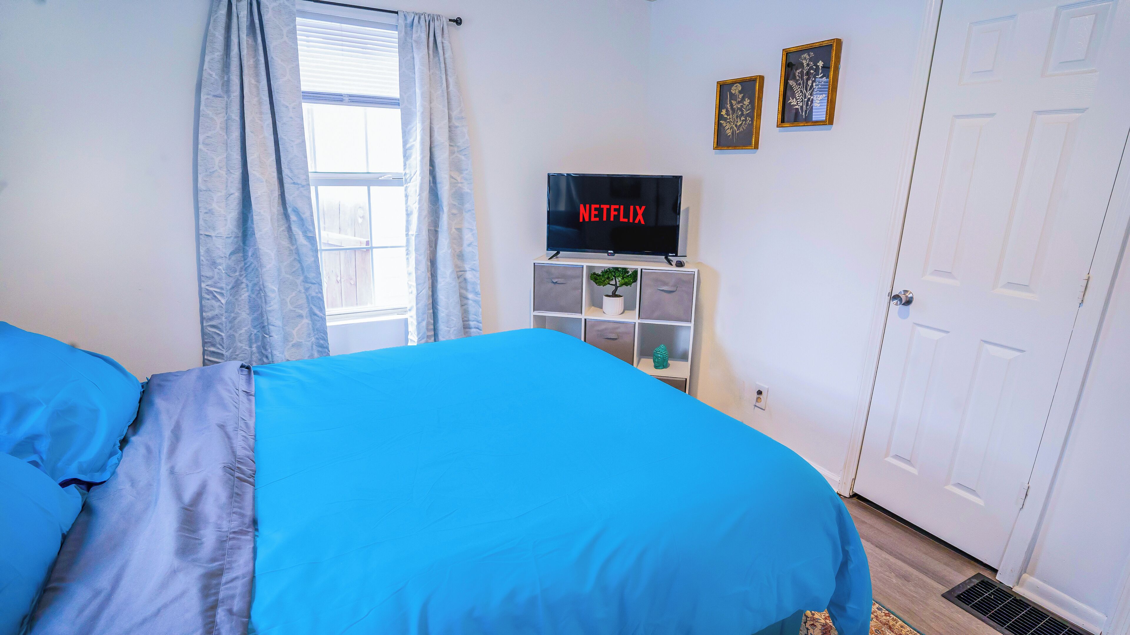 Een slaapkamer met twee bedden, een televisie op een standaard, een raam met gordijnen en een deur.