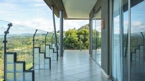 Een ruim balkon met glazen hekwerk en uitzicht op een weelderig landschap.