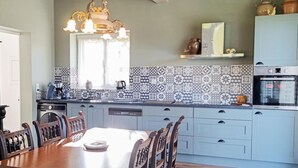 A kitchen with a dining table, chairs, a chandelier, a microwave, and patterned backsplash tiles.