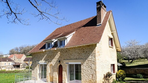 A stone house with a sloped roof, large windows, and a visible chimney.