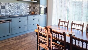 A kitchen with blue cabinets, a wooden dining table, and a chandelier.