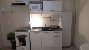 A compact kitchenette with a stove, microwave, and sink. - Air-conditioned studio, wifi in the center of Piratuba SC (Piratuba)