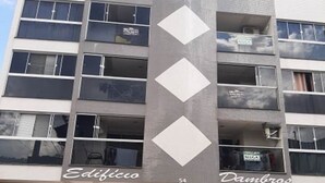 A multi-story building with a modern design, featuring a central column with diamond-shaped cutouts. The building has multiple balconies and large windows. The ground floor has a sign that reads "Edificio" and "Dambros". - Air-conditioned studio, wifi in the center of Piratuba SC (Piratuba)