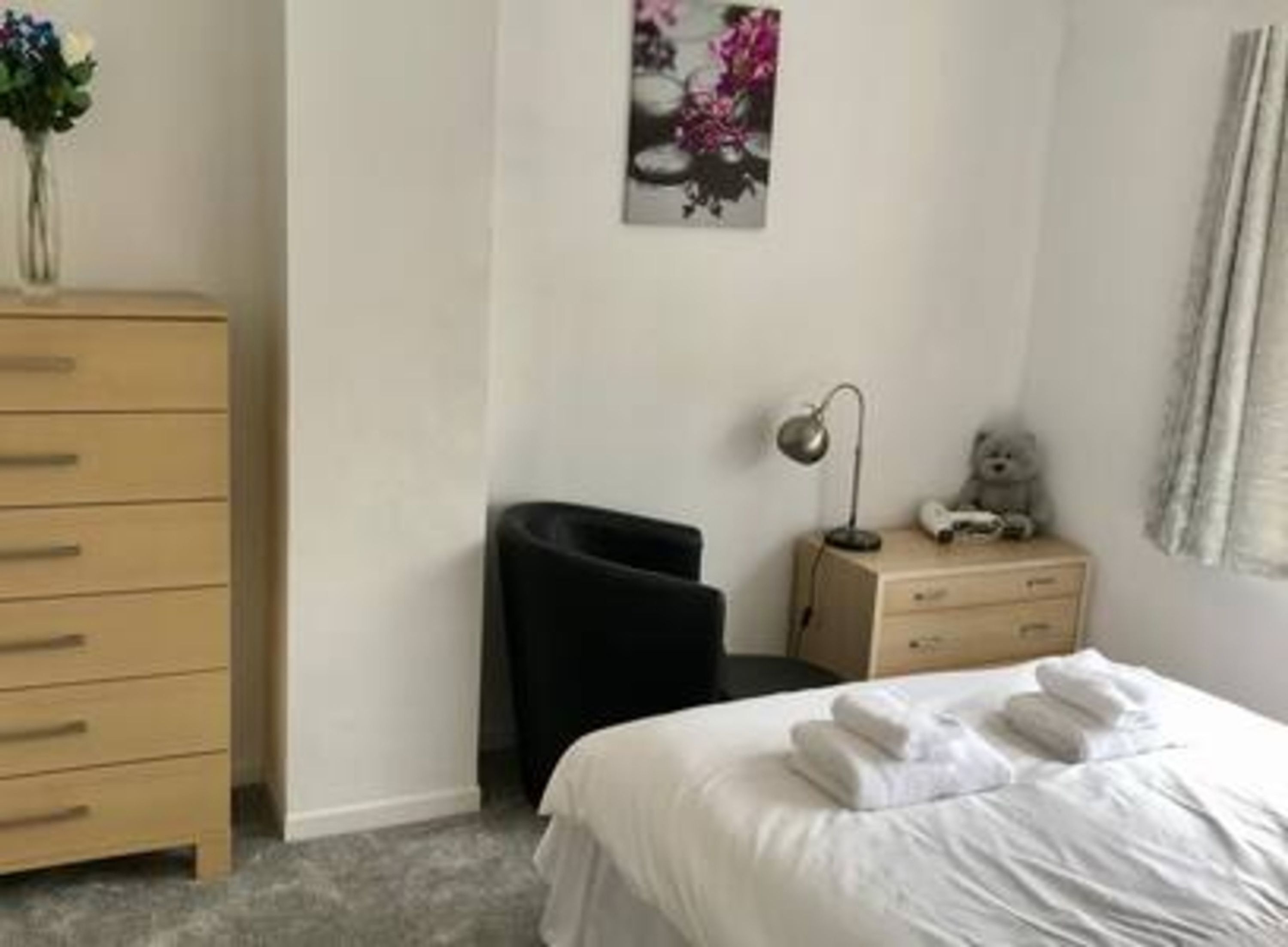 Une chambre d’hôtel avec un lit, une commode, un bureau, une chaise, une lampe et un ours en peluche.