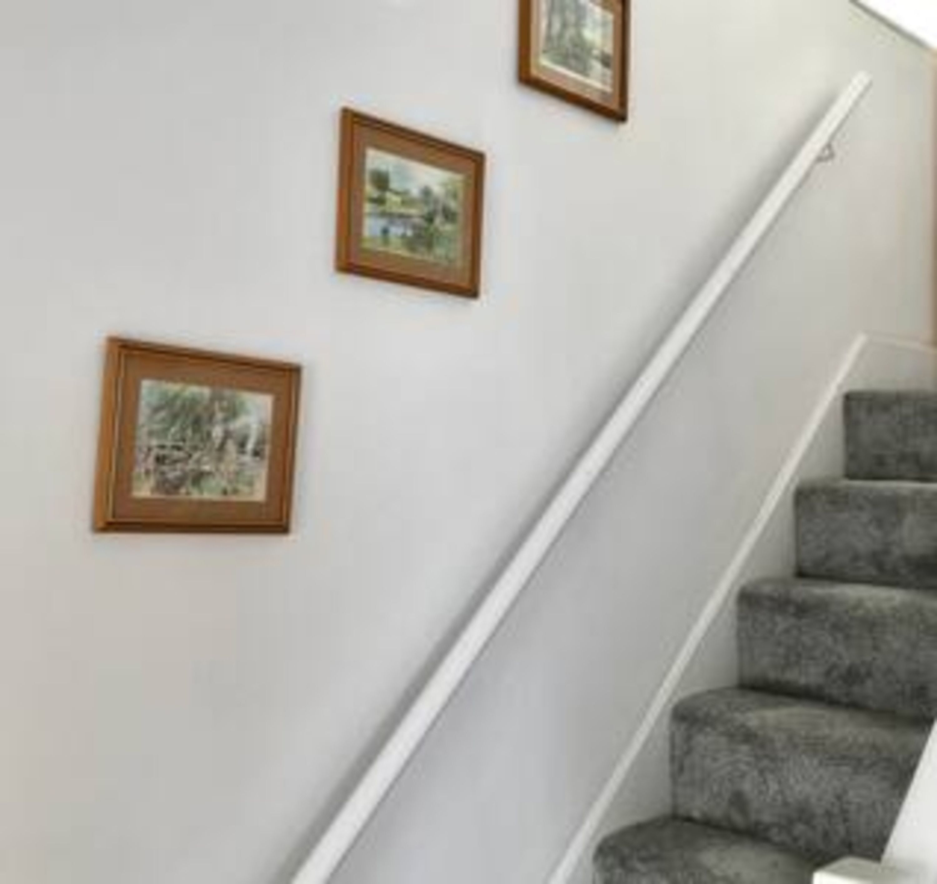 A staircase with a white handrail and grey carpeted steps. There are three framed pictures on the wall above the staircase.